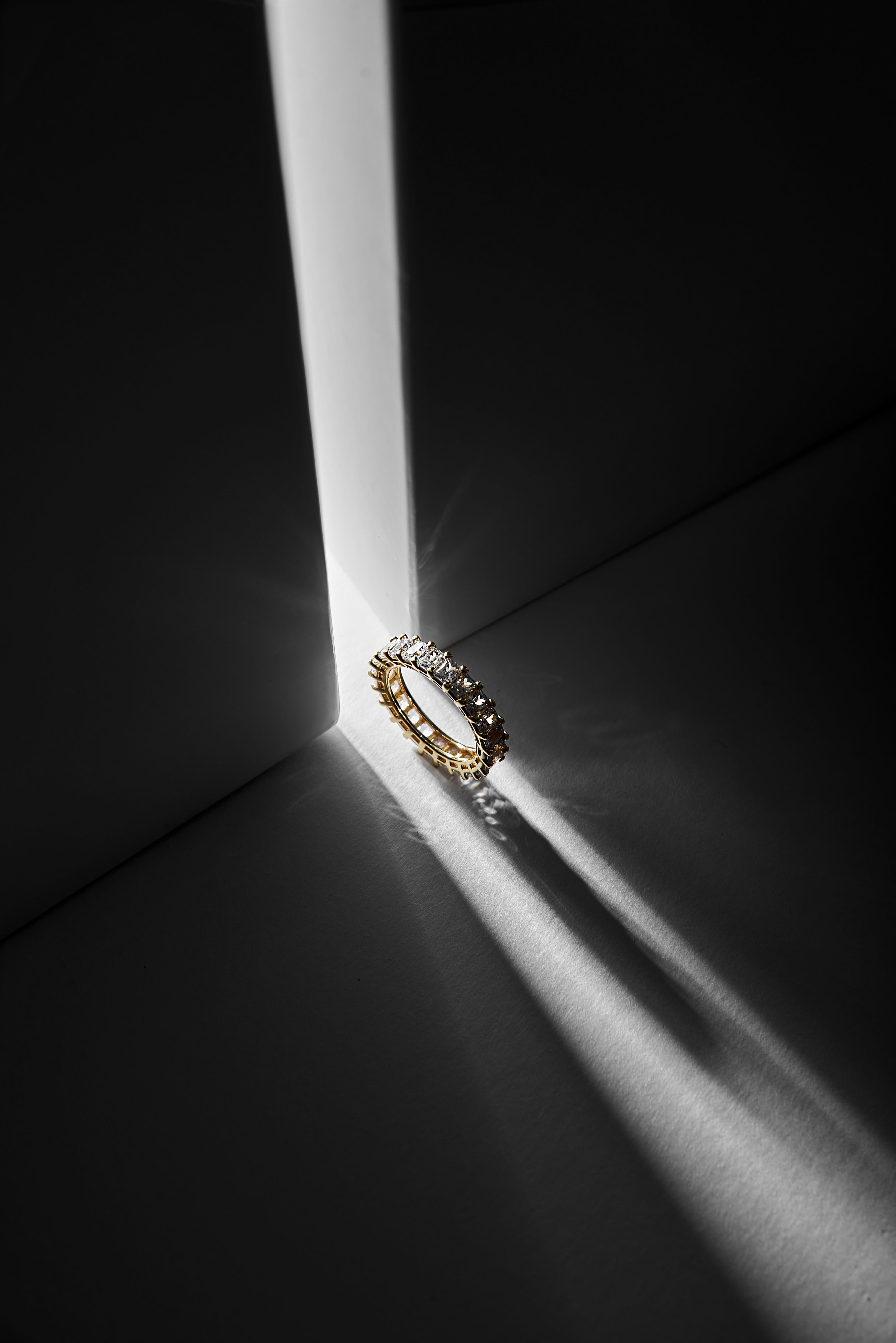 Gold diamond ring on a dark stone pedestal, in a shaft of light